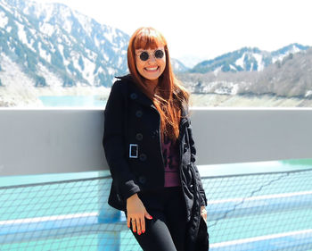 Portrait of a happy stylish woman standing against a bridge with a blurred mountain landscape behind 