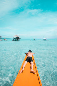 Rear view of shirtless man lying on boat deck over sea against cloudy sky