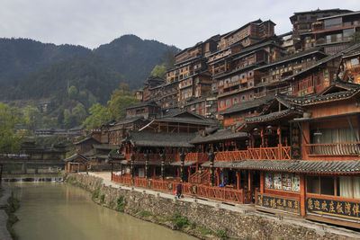 Traditional buildings by river against mountain