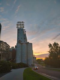 Road amidst buildings against sky during sunset