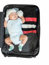 Full length of cute baby girl sleeping in suitcase against white background