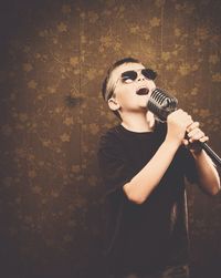 Boy wearing sunglasses while singing with microphone at home