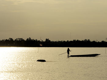 Silhouette person in sea against sky during sunset