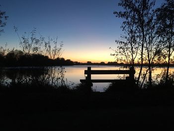 Silhouette trees by lake against sky during sunset