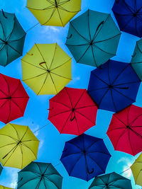 Low angle view of colorful umbrellas hanging against blue sky