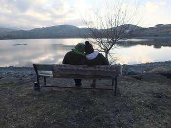 Rear view of couple sitting on lake against sky