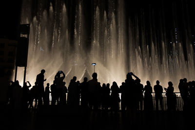 Silhouette people watching fountain show at night
