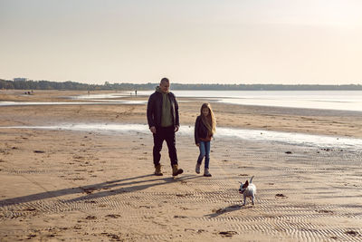 Father walks with daughter and dog near sea on sandy beach in afternoon in autumn. leather jackets