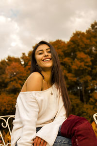 Portrait of smiling young woman with long hair sitting against trees