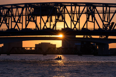 Silhouette bridge over river against sky during sunset