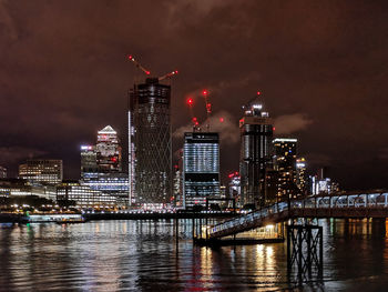 Illuminated buildings by river against sky at night