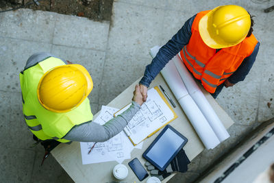 Woman and man in workwear shaking hands above construction plan