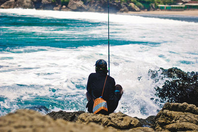 Rear view of man sitting on rock by sea