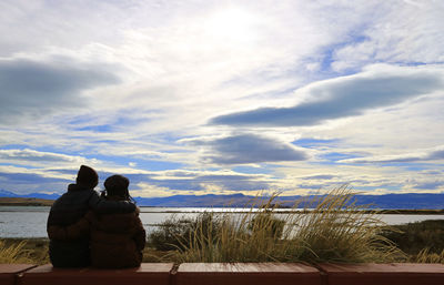 Rear view of couple sitting on bench against sky