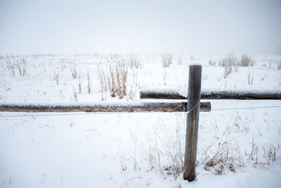 Snow covered land by fence on field during winter