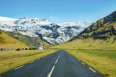 Diminishing empty road leading towards snowcapped mountain against clear blue sky