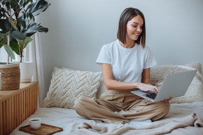 Young woman working on laptop at home in bed