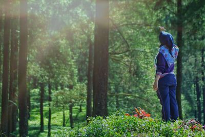 Rear view of woman standing by trees in forest