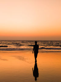 Silhouette man standing on beach against sky during sunset