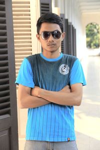 Portrait of young man wearing sunglasses while standing against wall