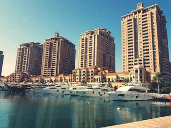 Boats moored in canal by buildings against clear sky