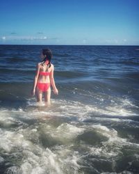 Rear view of girl standing at beach against sky