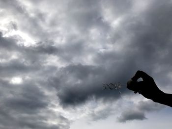 Low angle view of hand against cloudy sky