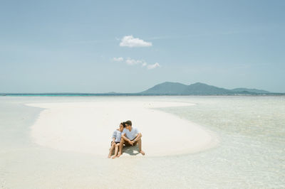 Man sitting on beach against sky