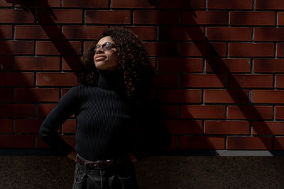 Portrait of young woman standing against brick wall