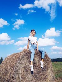 Full length of young woman sitting on hay bale in field