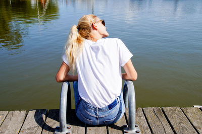 Rear view of young woman sitting on pier at harbor