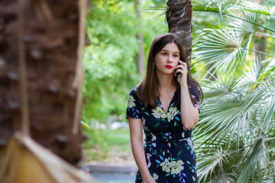 Young woman looking away while standing against trees