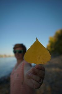 Woman holding yellow leaf while standing at beach