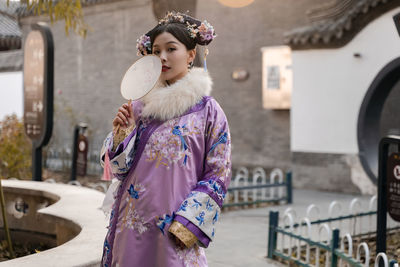 Portrait of woman wearing kimono holding mirror while standing outdoors