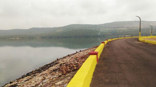 Yellow road by lake against sky