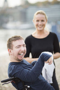 Disabled man on wheelchair laughing by caretaker outdoors