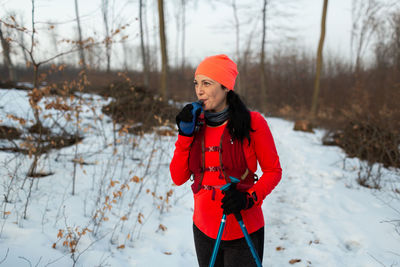 Female runner drinking water from soft flask in woods on winter day.