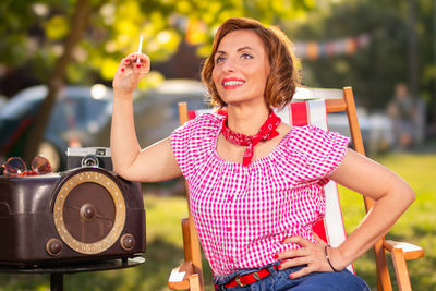 A smiling woman with a cigarette in her hand, dressed in pin-up style, poses leaning on radio