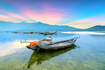 Fishing boat moored in lake against sky during sunset