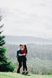 Side view of loving young couple standing against sky in forest during sunny day