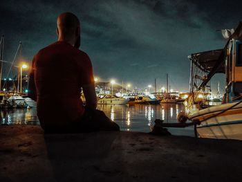 Rear view of man sitting on pier at harbor