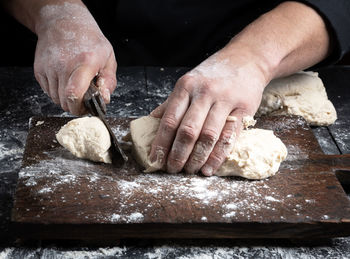 Cropped hands of chef cutting dough