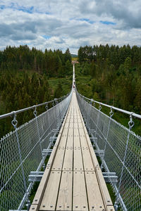 Footbridge amidst trees in forest against sky