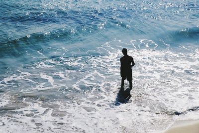 High angle view of silhouette man standing in shallow water at sea