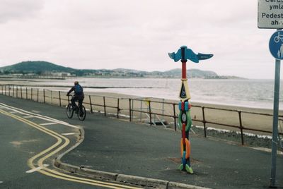 Man riding bicycle on road by sea against sky