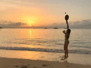 Side view of woman in bikini playing matkot at beach during sunset