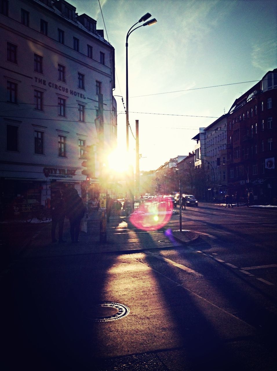 building exterior, architecture, built structure, street, sun, transportation, sunlight, lens flare, car, city, sunbeam, mode of transport, street light, land vehicle, road, sunset, sky, building, city street, outdoors