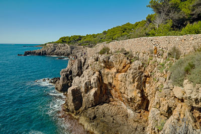 Rock formations by sea against clear blue sky