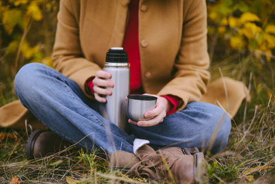 Low section of woman holding coffee while sitting outdoors