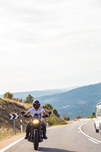 Young man riding motorcycle on road against sky